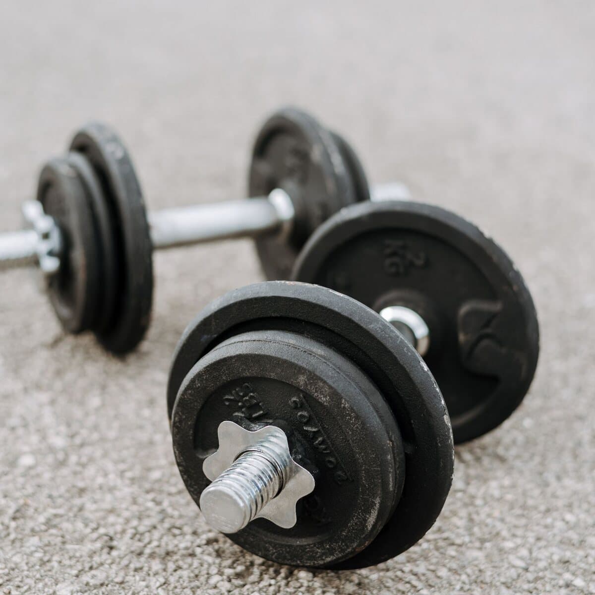 A pair of cast iron dumbbells with spare plates and collars, on a concrete floor